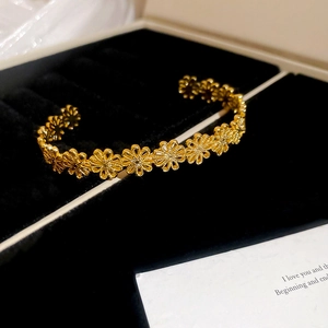 Detail shot of golden floral open bangle with intricate petal texture on black velvet