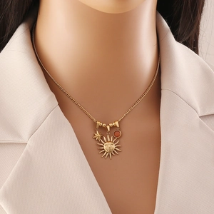 Gold stainless steel necklace with sun and star pendants worn over a beige suit lapel
