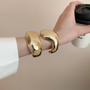 Primo piano di bracciali geometrici in oro lucido con finitura a specchio riflettente