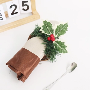 Rond de serviette de Noël avec feuilles de houx, baies rouges et vigne sur une table blanche