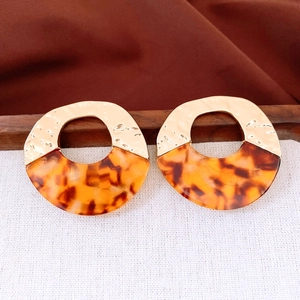 Detail of tortoiseshell acrylic and textured gold metal round earrings on linen