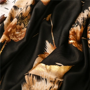 Detail of soft silk-touch scarf with golden feather pattern on elegant black fabric