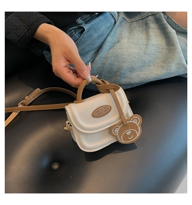 Close-up of white and khaki mini crossbody bag with cute bear charm and logo detail