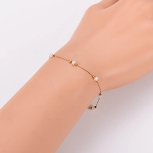 Elegant gold chain bracelet with white beads and stars on woman's wrist, white background