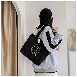 Detail of black corduroy tote bag with rabbit embroidery and cute cow charm on a model