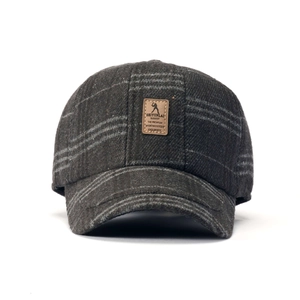 Dettaglio cappello a quadri grigio scuro con toppa in pelle marrone sulla parte frontale