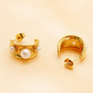 Elegant gold C-shaped earrings with three pearls on a silk fabric background