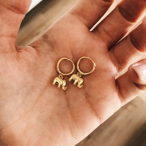 Close-up of small golden hoop earrings with detailed elephant charms held in palm