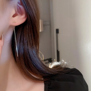 Détail de boucles d'oreilles pendantes en or portées par un mannequin au style épuré