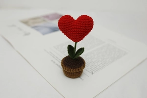 Macro shot of handmade crochet red heart plant in a brown knitted pot on a magazine