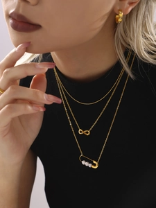Détail du collier doré à trois rangs avec breloque infini et épingle de sûreté à perles