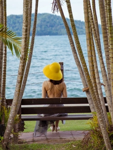 Detail of a large yellow sun hat paired with an open-back dress against a seaside view