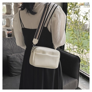 Detailed texture of white lychee leather camera bag with striped wide shoulder strap