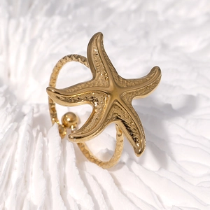 Adjustable gold starfish ring with textured rope band on white coral background