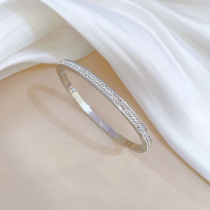 Macro detail of silver titanium steel bangle with multi-row pave crystals on white silk