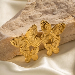 Detailed view of layered gold butterfly earrings resting on white silk and textured stone