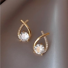 Close-up of gold-plated crossover stud earrings featuring a large round center zircon