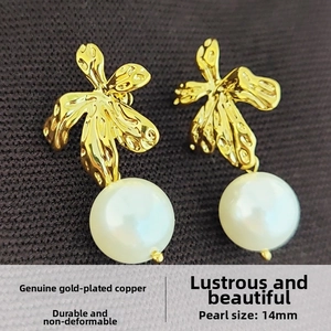 Macro detail of leaf-shaped gold plated earrings featuring 14mm round white pearls
