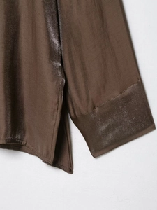Detail of brown silk shirt featuring smooth cuffs and elegant side slit hemline design