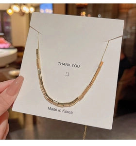 Close-up of minimalist gold cylinder tube pendant necklace on Thank You display card