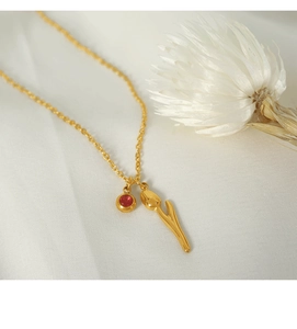 Detail of 18k gold plated tulip necklace with red crystal pendant on white silk