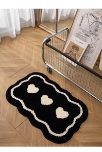 Close-up of black irregular fluffy bath mat with white hearts on light wooden floor