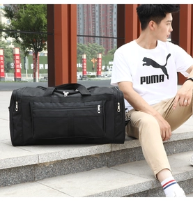 Close-up of a large black foldable travel duffel bag held by a model in an outdoor setting