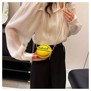 Close-up of a mini yellow basketball crossbody bag with a gold chain strap on a white shirt