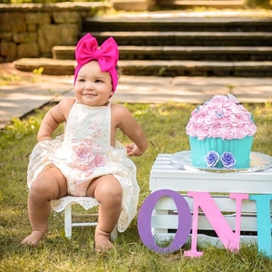 Detailed shot of baby girl lace romper with fuchsia bow headband on outdoor lawn