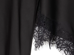 Detail of black silk-like fabric with delicate eyelash lace trim on an asymmetric skirt