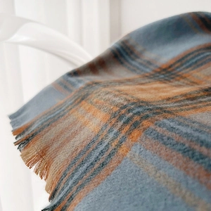 Detail of plaid winter scarf with fringe, featuring blue and orange soft cashmere texture