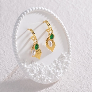 Detailed macro shot of vintage gold earrings with green teardrop gems and white pearls