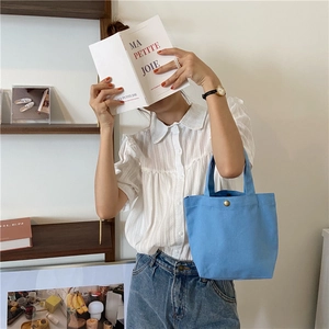 Detailed shot of a blue canvas tote bag held by a model in a minimalist French cafe setting