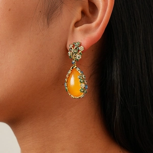 Détail de boucles d'oreilles vintage en résine avec fleurs en zircon et goutte orange vif