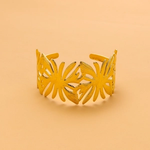 Detailed close-up of a wide golden cuff bracelet featuring an intricate cutout leaf design