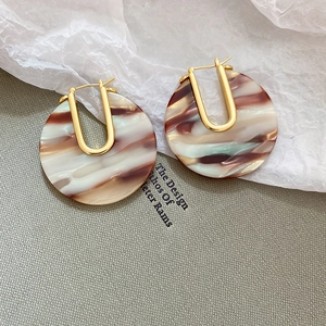 Détail macro de boucles d'oreilles dorées en U avec disques ronds en acétate écaille