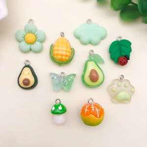 Flat lay of green resin DIY charms including avocado, cat paw, and butterfly pendants