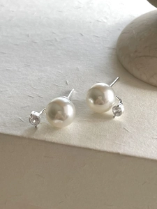 Detailed view of sterling silver pearl and zircon earrings on a minimalist cream base