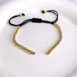 Detail of adjustable black woven bracelet with polished gold beads on a white tray