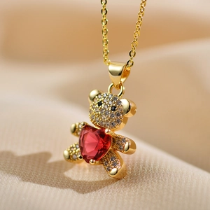 Close-up of golden teddy bear pendant featuring a red heart gemstone and micro-pave zircons