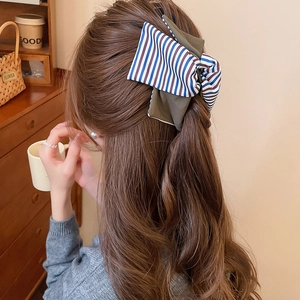 Détail d'une grande pince à cheveux à nœud rayé tricolore sur un chignon de femme