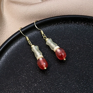 Close-up of beaded drop earrings with red and green beads on a black ceramic plate