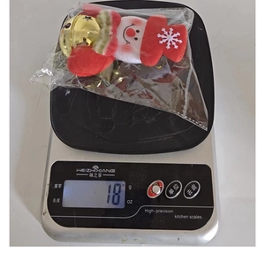 Close-up of a Christmas snowman plush bell ornament being weighed on a scale, showing 18g