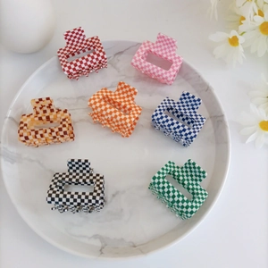 Detail of seven checkered hair claws in various colors on a marble tray with daisies