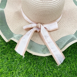 Détail d'un chapeau de paille beige avec bord en dentelle verte et ruban décoratif
