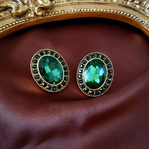 Close-up of vintage oval emerald studs with gold frames on dark silk background