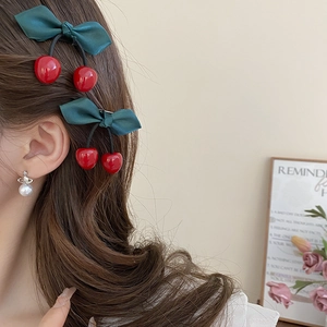 Detail of sweet cherry bow hair clips and planet pearl earrings worn by a model