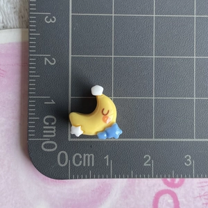 Macro view of a miniature yellow crescent moon resin accessory with a blue star on a grid mat