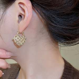 Macro shot of gold heart-shaped hoop earrings with intricate woven mesh texture on a model