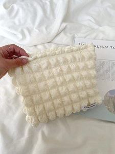 Close-up of cream waffle-textured makeup bag with ruffled edges and lovely text label